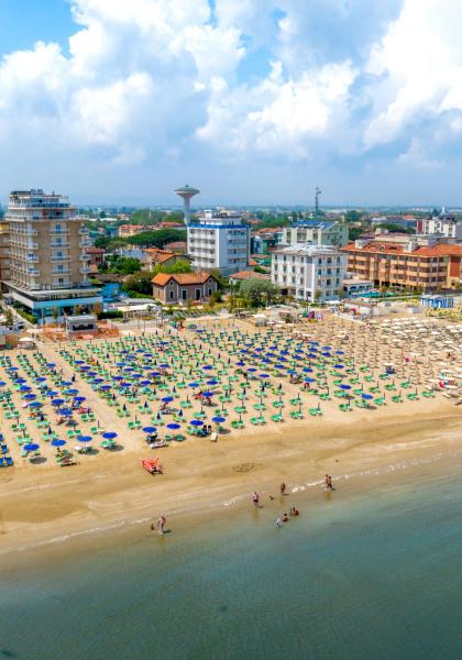 Belebter Strand mit bunten Sonnenschirmen und Gebäuden im Hintergrund.