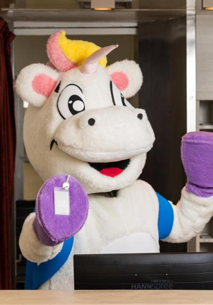 Einhorn-Maskottchen hinter einem Empfangstresen mit lila Handschuhen.