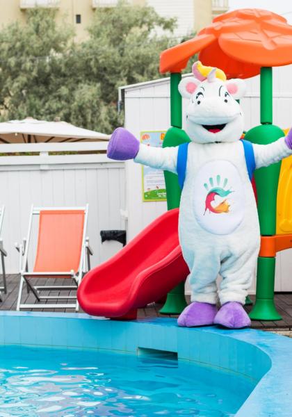 Einhorn-Maskottchen neben Pool und buntem Rutsche.