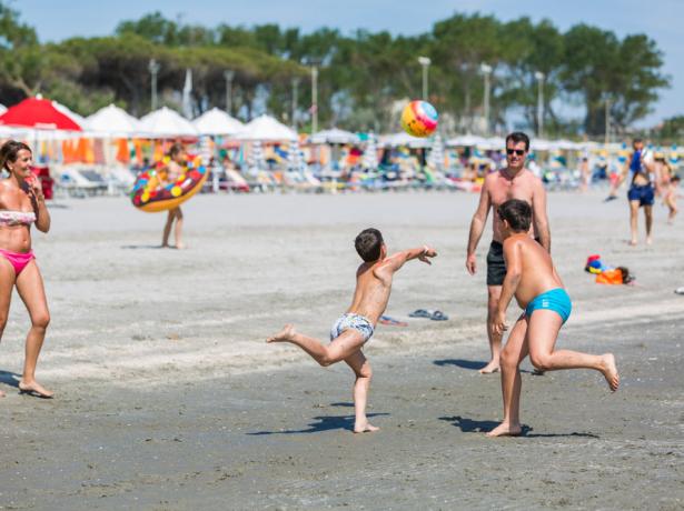 Famiglia gioca a palla sulla spiaggia in una giornata di sole.