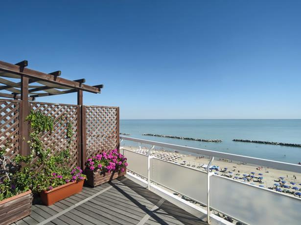 Terrace with sea view, flowers, and crowded beach.