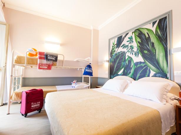 Chambre d'hôtel avec lit double et lits superposés, décorée de feuilles tropicales.