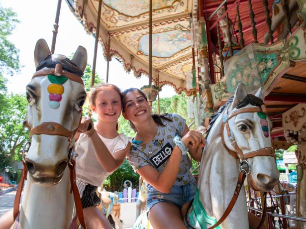 Deux filles souriantes sur un carrousel coloré, entourées d'une ambiance joyeuse.