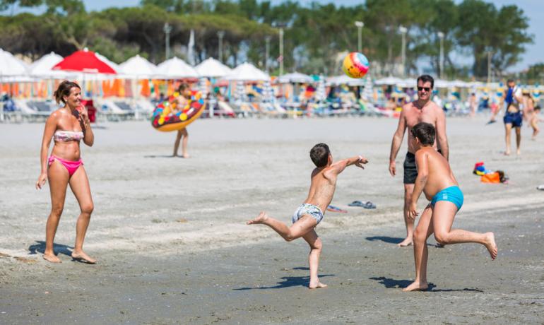 Famiglia gioca a palla sulla spiaggia in una giornata di sole.