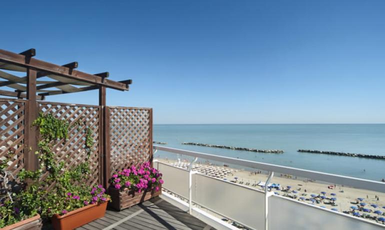 Terrasse mit Meerblick, Blumen und belebtem Strand.