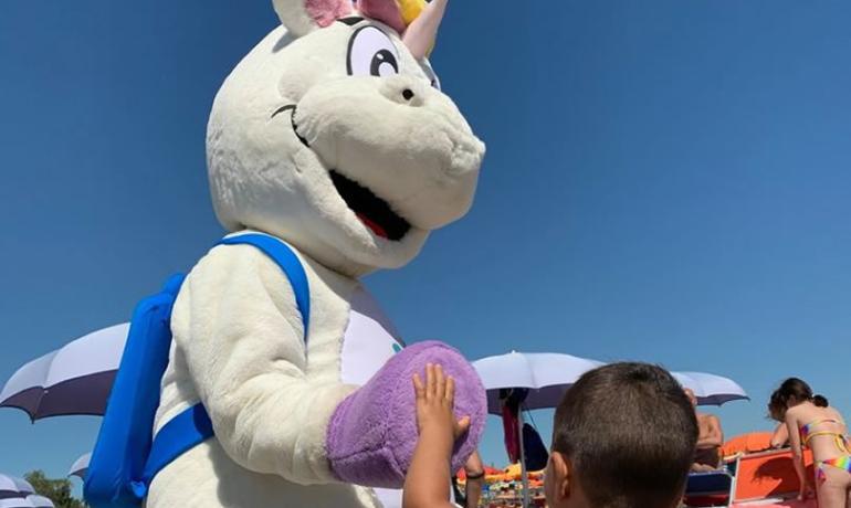 Un costume da unicorno interagisce con un bambino in spiaggia.