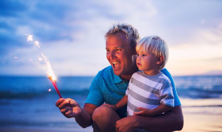 Vater und Sohn sehen Funken am Strand bei Sonnenuntergang.