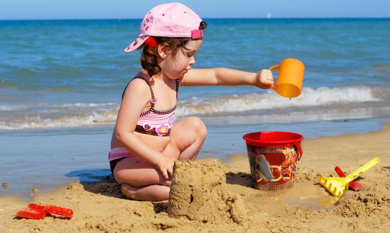 Bambina gioca sulla spiaggia con secchio e paletta.