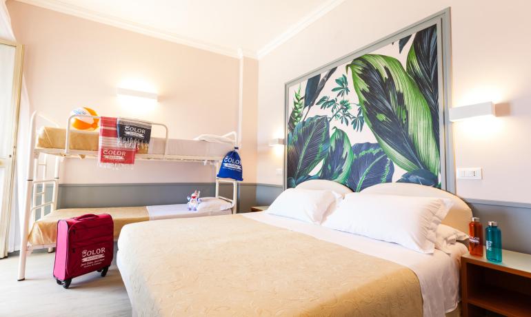 Hotelzimmer mit Doppelbett und Etagenbetten, dekoriert mit tropischen Blättern.
