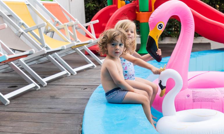 Bambini che giocano in piscina con gonfiabili colorati.