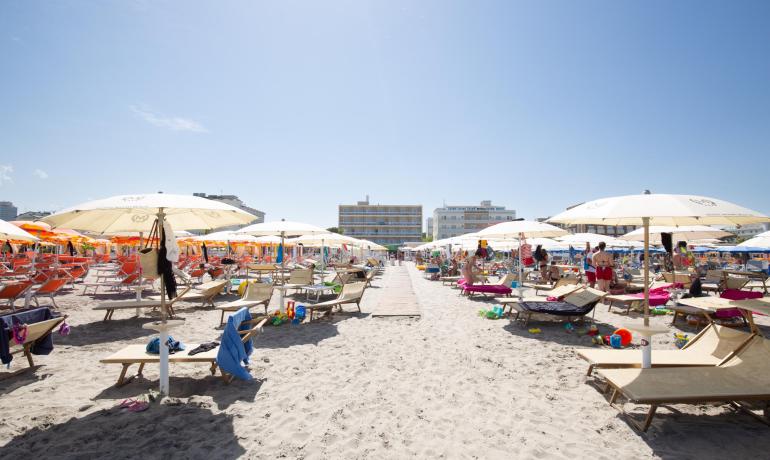 Überfüllter Strand mit Sonnenschirmen und Liegen unter blauem Himmel.