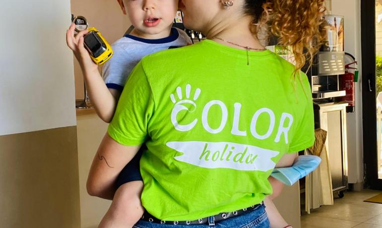 Donna con bambino in braccio, maglietta verde e pantaloncini di jeans.