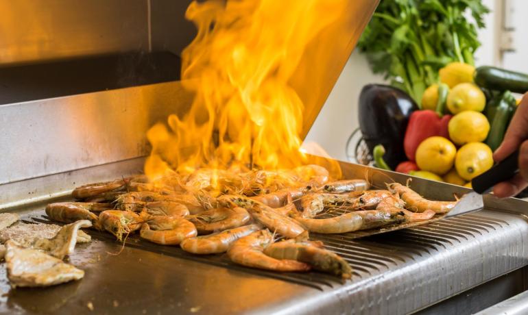 Gegrillte Garnelen mit Flammen, frisches Gemüse im Hintergrund.
