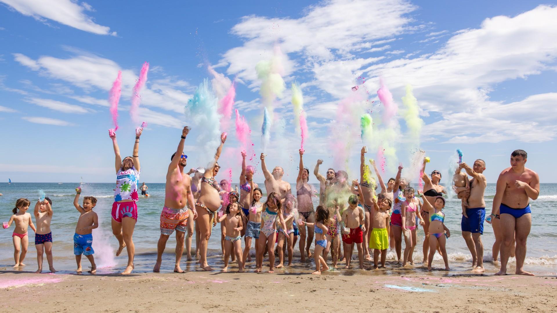 Des gens lancent des poudres colorées sur la plage par une journée ensoleillée.