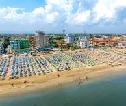 Spiaggia affollata, ombrelloni colorati, mare calmo, cielo azzurro, atmosfera vivace.