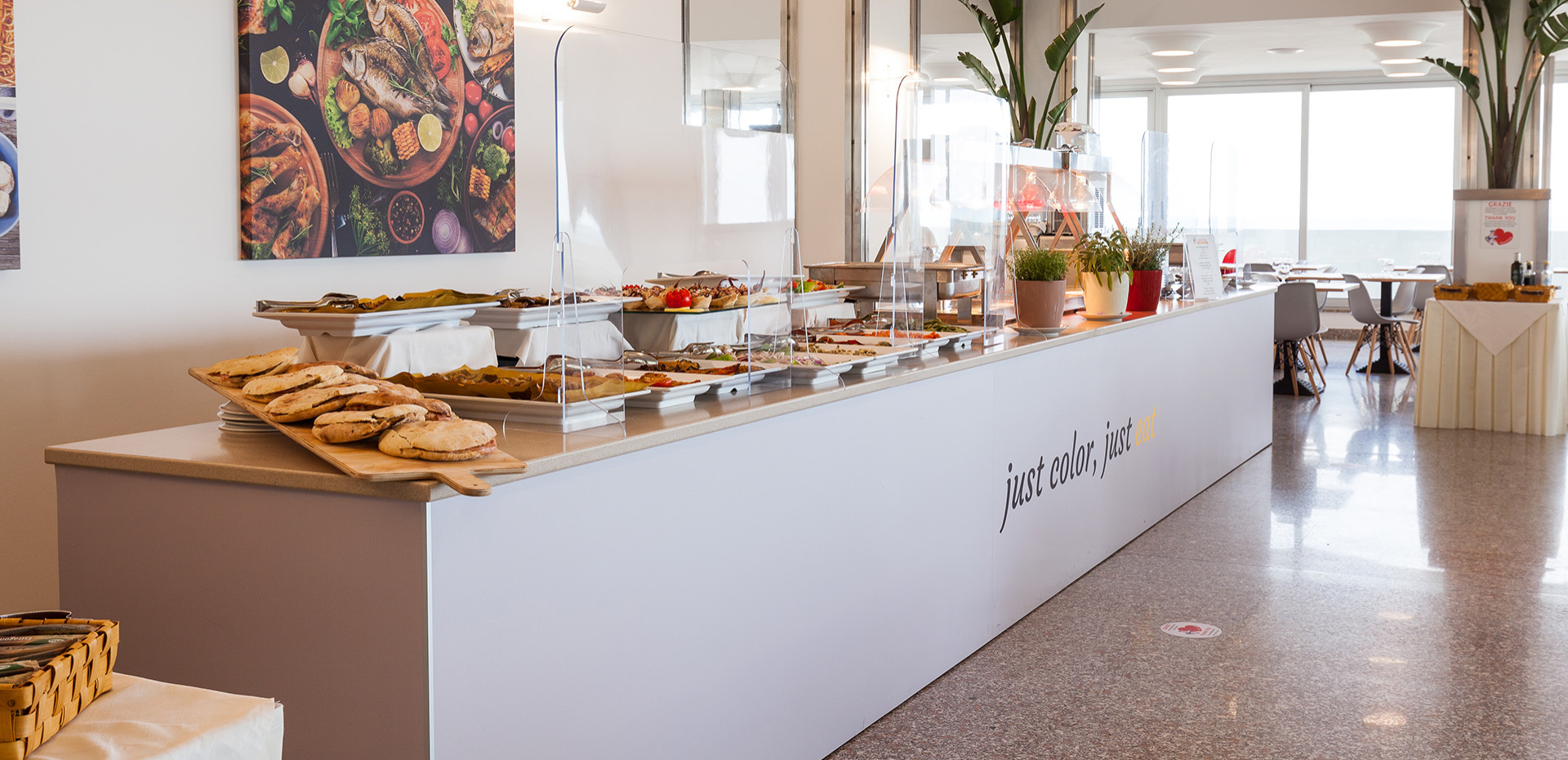 Ristorante luminoso e moderno con tavoli apparecchiati e area buffet.