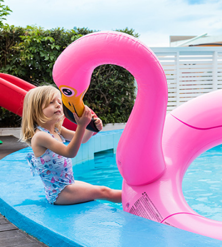 Happy child plays with pink inflatable flamingo by the pool.