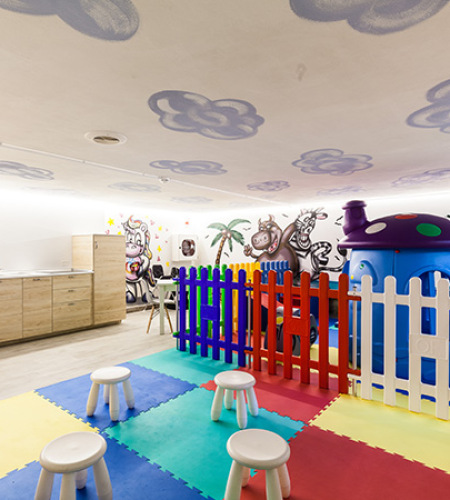Area giochi per bambini con scivolo giallo e sedie colorate.