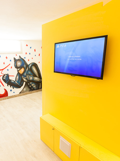Sala giochi con supereroi, TV e arredi colorati per bambini.