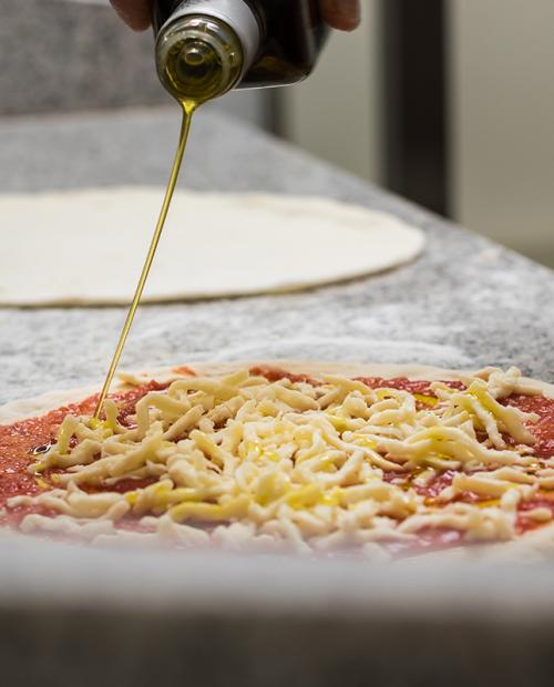 Pizza cruda con olio d'oliva, formaggio e salsa di pomodoro su piano di lavoro.