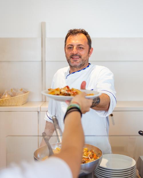 Cuoco sorridente serve pasta con calore e gentilezza.