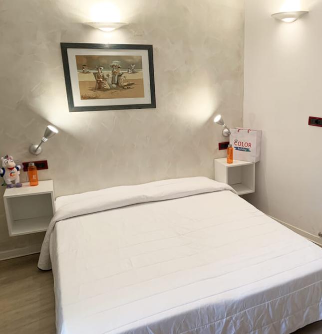 Stanza accogliente con letto bianco, decorazioni giocose e valigia rossa.