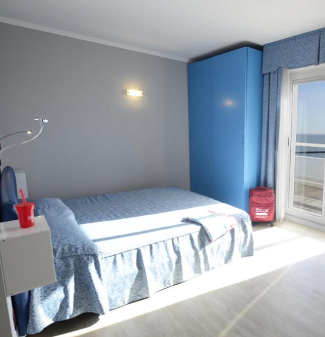 Camera luminosa con vista mare, arredi blu e atmosfera rilassante.