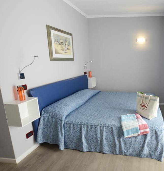 Camera accogliente con letto blu, luce calda e atmosfera rilassante.