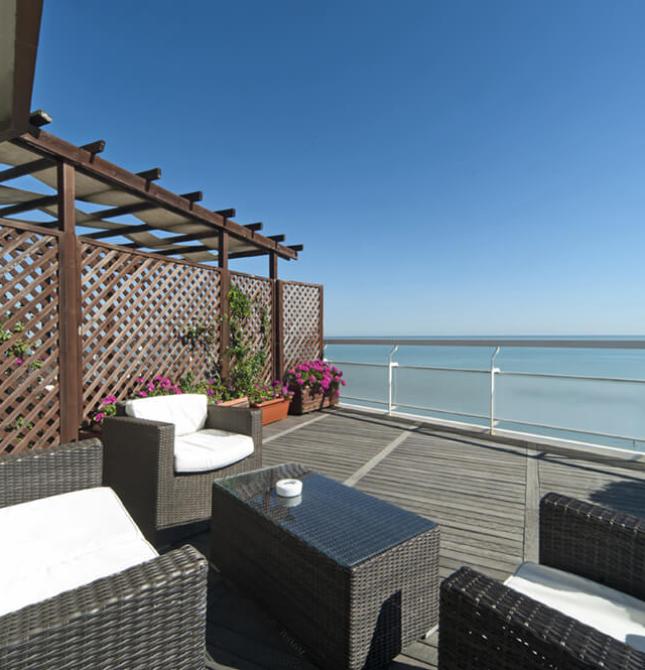 Terrazza elegante con vista mare, arredi confortevoli e cielo sereno.