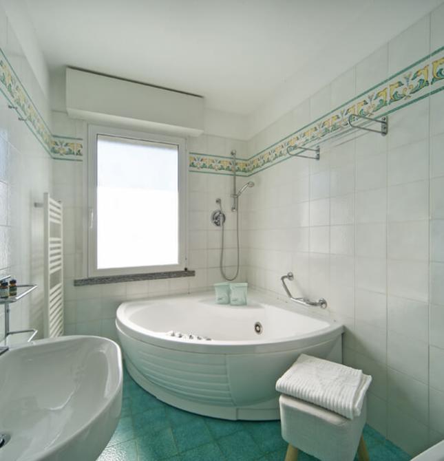 Bagno luminoso con vasca angolare, piastrelle eleganti e atmosfera rilassante.