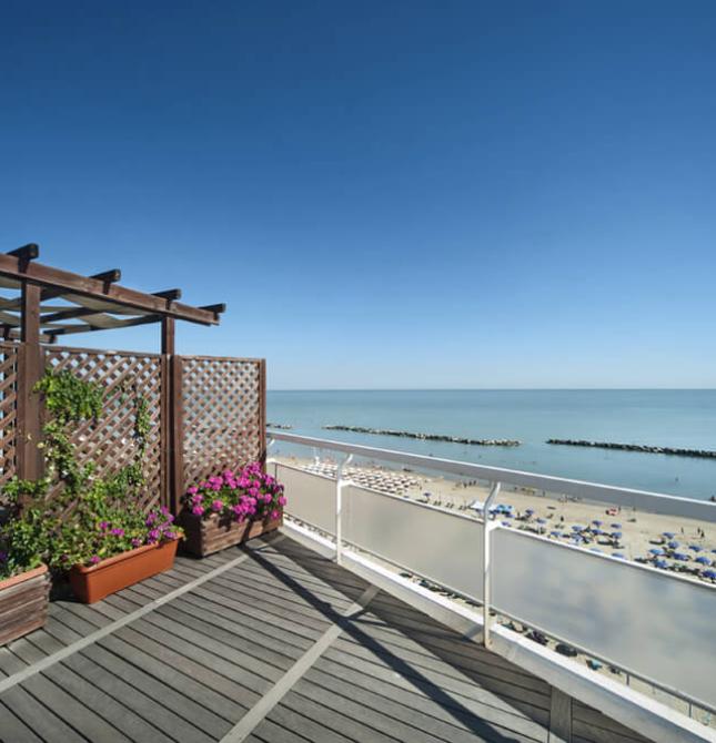 Terrazza fiorita con vista mare e spiaggia, cielo limpido e sereno.